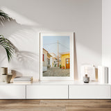 A framed print of 'Siesta in Samos' hanging in a bright, airy living room with Mediterranean decor.