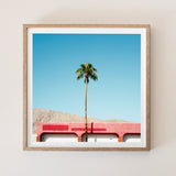 Minimalist Palm Springs photography print titled Red by John Trif, featuring a lone palm tree against a vibrant crimson architectural wall and desert mountains.